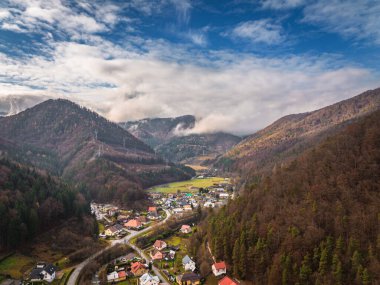 Kuzey Slovakya 'da Stankovany yakınlarındaki kırsal bir dağ vadisinin sonbahar manzarası. Mala Fatra ve Sipska Fatra dağları arasında küçük köyler, virajlı yollar ve ormanlık tepeler bulunur. Renkli sonbahar yaprakları, dramatik bulutlar ve barışçıl coun