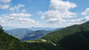 Slovakya 'nın Mala Fatra dağlarındaki Maly Rozsutec zirvesinden yaz mevsimi manzarası. Işık bulutları dinamik bir şekilde ormanlık dağ sırtları ve derin vadilerin üzerindeki mavi gökyüzünde hareket eder. Parlak yaz ışığı ve berraklık.