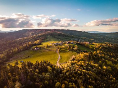 Beskid Zywiecki 'de Hala Boracza' nın hava sonbahar günbatımı manzarası. Sıcak altın ışık ormanlık tepeleri, dağ çayırlarını ve dolambaçlı yollarla birbirine bağlı kırsal binaları aydınlatır. Karpatlar 'daki huzurlu kırsal alan