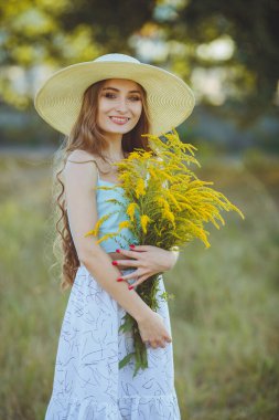 Doğada bir buket kır çiçeğiyle şapkalı güzel bir kız.