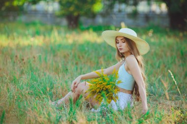 Doğada bir buket kır çiçeğiyle şapkalı güzel bir kız.