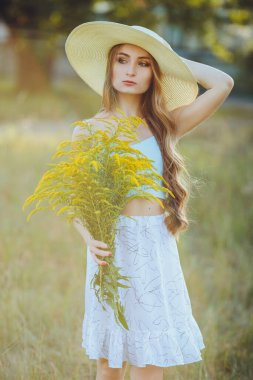 Doğada bir buket kır çiçeğiyle şapkalı güzel bir kız.