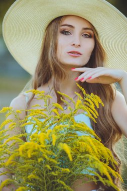 Doğada bir buket kır çiçeğiyle şapkalı güzel bir kız.