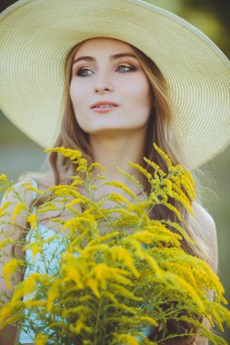 Doğada bir buket kır çiçeğiyle şapkalı güzel bir kız.