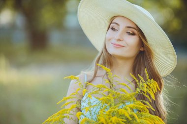 Doğada bir buket kır çiçeğiyle şapkalı güzel bir kız.