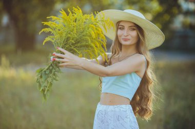 Doğada bir buket kır çiçeğiyle şapkalı güzel bir kız.