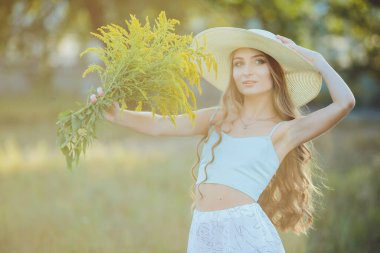 Doğada bir buket kır çiçeğiyle şapkalı güzel bir kız.