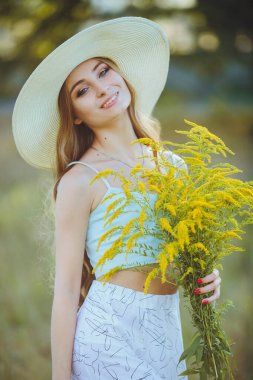 Doğada bir buket kır çiçeğiyle şapkalı güzel bir kız.