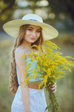 Doğada bir buket kır çiçeğiyle şapkalı güzel bir kız.