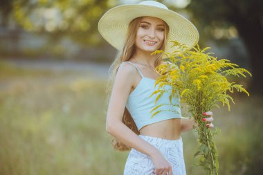 Doğada bir buket kır çiçeğiyle şapkalı güzel bir kız.