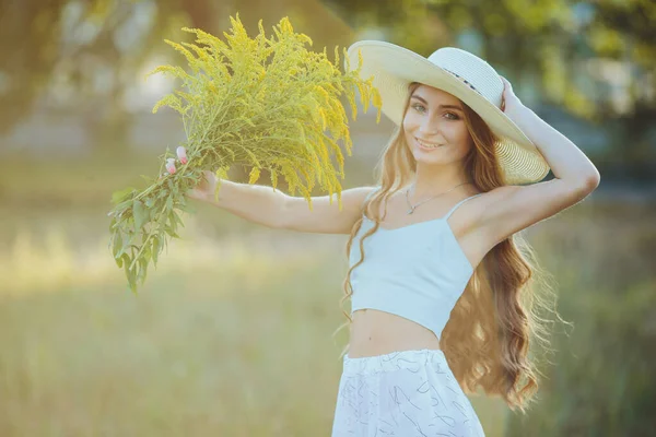 Doğada bir buket kır çiçeğiyle şapkalı güzel bir kız.