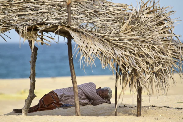 Old man resting in shadow in Sri Lanka beach