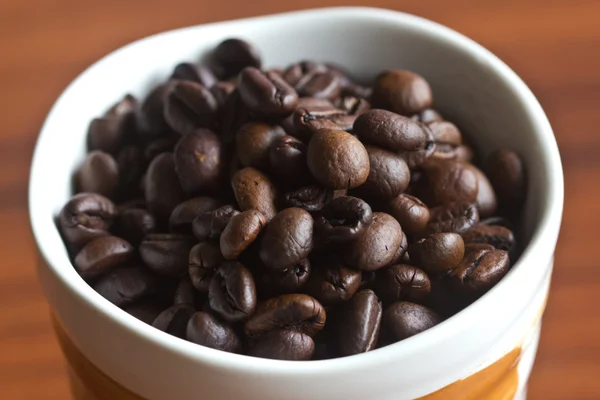 Kaffeebohnen in einer Tasse auf einem Holztisch — Stockfoto