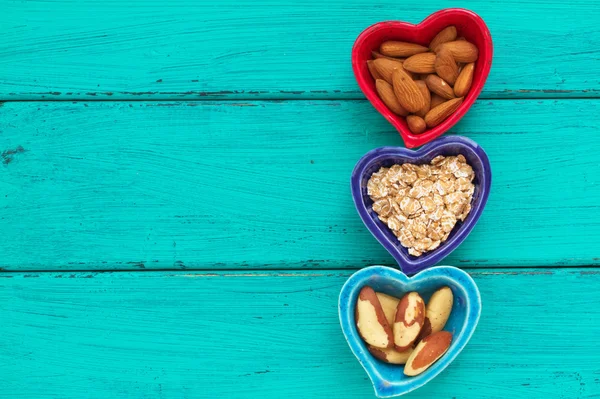 Ceramic heart shape bowls with healthy breakfast items: whole oatmeal, almonds and Brazil nuts — Stock Photo, Image