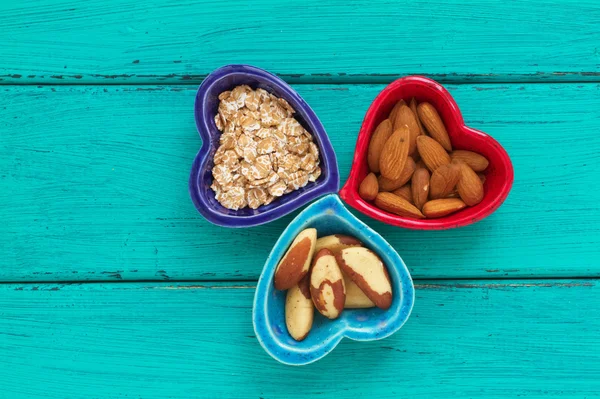 Ceramic heart shape bowls with healthy breakfast items: whole oatmeal, almonds and Brazil nuts — Stock Photo, Image