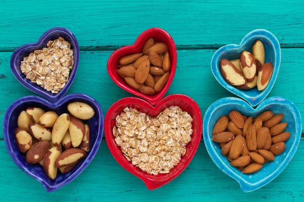 Ceramic heart shape bowls with healthy breakfast items: whole oatmeal, almonds and Brazil nuts