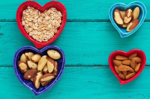 Ceramic heart shape bowls with healthy breakfast items: whole oatmeal, almonds and Brazil nuts — Stock Photo, Image