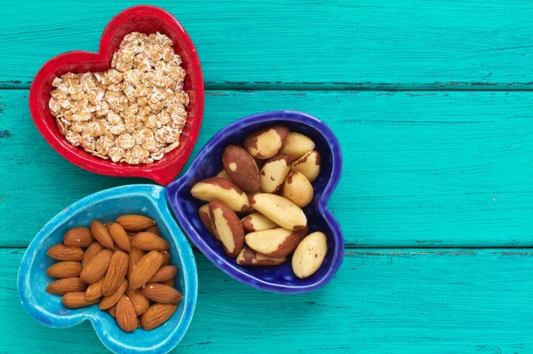 Ceramic heart shape bowls with healthy breakfast items: whole oatmeal, almonds and Brazil nuts — Stock Photo, Image