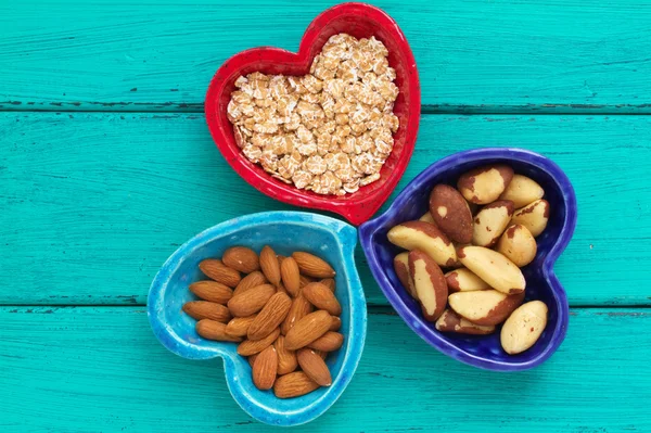 Ceramic heart shape bowls with healthy breakfast items: whole oatmeal, almonds and Brazil nuts — Stock Photo, Image