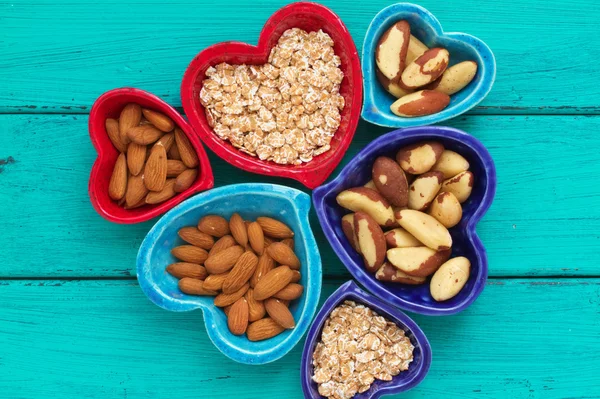 Керамические миски в форме сердца со здоровыми предметами для завтрака: овсянка, миндаль и бразильские орехи — стоковое фото