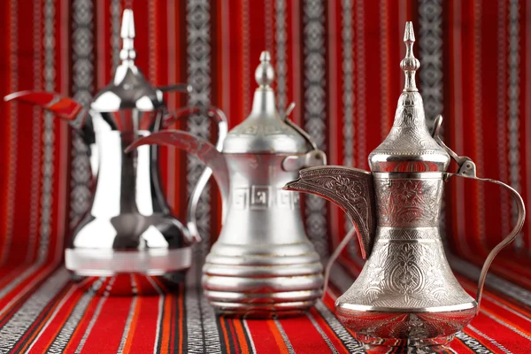 Três panelas Dallah ornamentados são colocados em tecido vermelho tradicional do Oriente Médio — Fotografia de Stock