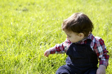 Küçük çocuk çimenlerde oturuyor.