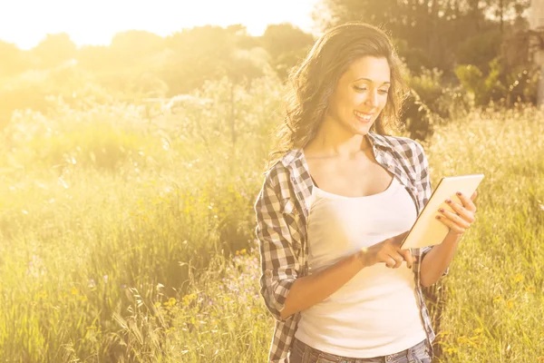 Smiling girl in a field of flowers working on tablet — Stock Photo, Image