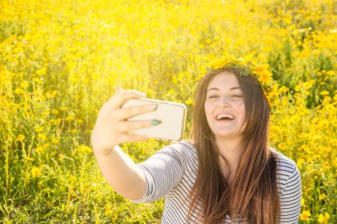Güzel ve hoş bir kız cep telefonuyla kendi portresini çekerken gülüyor.