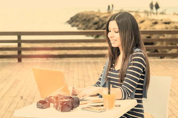 Young woman working on laptop by the sea warm filter applied