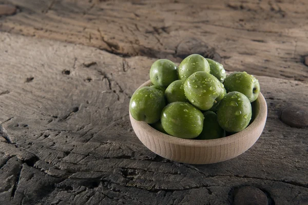 Green olives into wood pot on an old wooden table — Stock Photo, Image