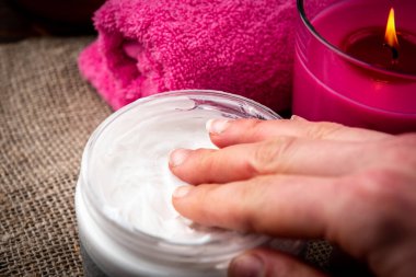 Kadın eli krema alır. Ahşap arka planda pembe aromalı mum ve havlunun spa bileşimi