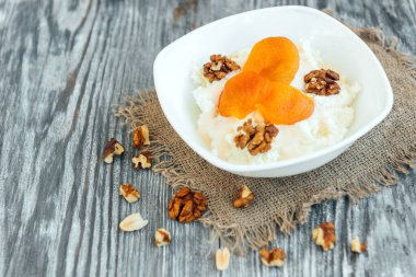 Ekşi kremalı süzme peynir, kuru kayısı ve gri ahşap arka planda ceviz..