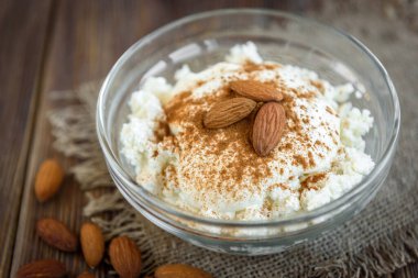 Ekşi kremalı süzme peynir, koyu ahşap arka planda tarçın ve badem. Sağlıklı diyet yemekleri. Protein yemeği..