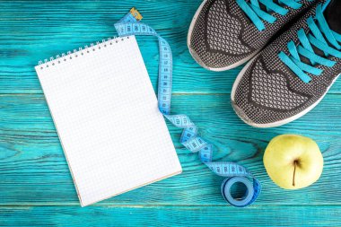 Spor geçmişi: bant, defter ve elma mavi ahşap arka planda. Fitness, sağlıklı yaşam tarzı, egzersiz planı.