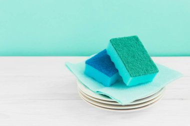 Bir şişe bulaşık, sünger, ahşap masadaki çatal bıçak yeşil bir duvar zeminine dayanır.