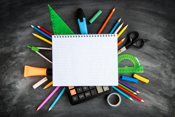 School supplies on black board background. Color pencils, calculator, rules and copybooks. Back to school concept. 1of September.