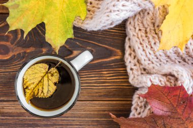 Bir kupa kahve, sonbahar yaprakları ve koyu ahşap arka planda eşarp. Merhaba sonbahar konsepti.