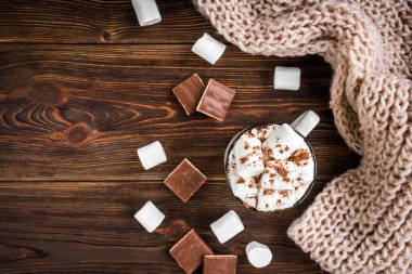 Marşmelovlu sıcak içecek, çikolata ve koyu ahşap arka planda örülmüş eşarp.