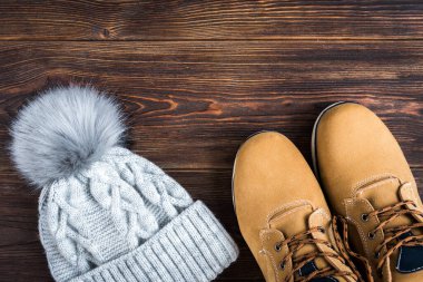 Gri kış örgü şapka ve ahşap arka planda sarı çizmeler..