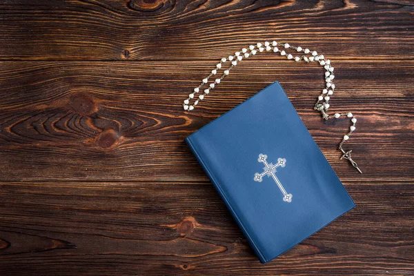 Open bible, candle, christian cross and human hands on wooden background. Prayer to God.
