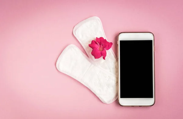 Woman hygiene protection. Sanitary pads with pain pill, pink rose and mobile phone on pink background. Menstrual cycle tracking.