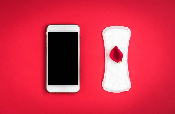 Woman hygiene protection or sanitary pads with rose petals and mobile phone on red background. Menstrual cycle tracking.