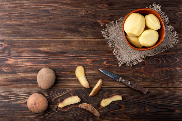 Stock image Raw peeled potatoes in bowl on dark wooden background.