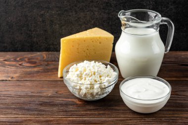 Koyu ahşap arka planda süt ürünleri. Süt, kefir, peynir, süzme peynir, tereyağı ve ekşi krema..