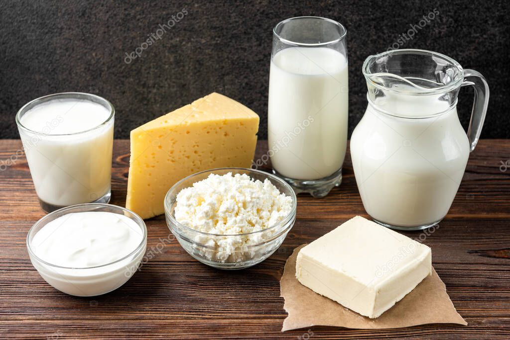 Dairy products on dark wooden background. Milk, kefir, cheese, cottage cheese, butter and sour cream.