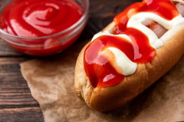 Siyah ahşap arka planda mayonez ve ketçap sosisli sandviç..