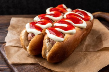 Siyah ahşap arka planda mayonez ve ketçap sosisli sandviç..