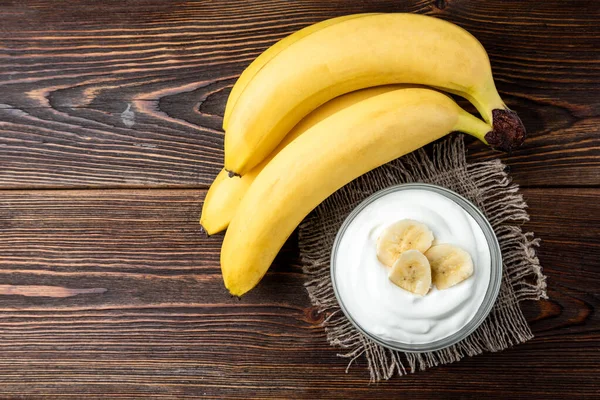 Banana and yogurt on dark wooden background.