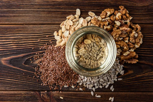 Walnut, peanut, sunflower and flax seeds on dark wooden background.