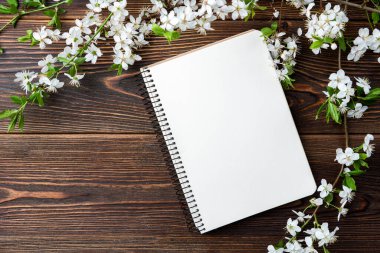 Bahar çiçekleri kiraz dalları ve koyu ahşap arka planda bir defter..